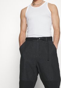 Svarta, lösa byxor med en strukturerad yta, justerbart bälte och sidofickor, i kombination med en vit linne.