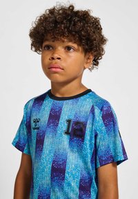 Ung dreng med krøllet hår iført blå sportsjersey med nummer 12, kigger let op og mod højre.