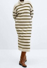 Langes beiges Strickkleid mit dunkelolivgrünen Streifen, ausgestattet mit einem Rollkragen und einem lässigen Schnitt. Kombiniert mit braunen Lederstiefeln bis zu den Knien.