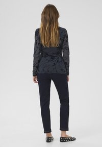 Langarmige marineblauwe top met bloemachtige textuur, gecombineerd met donkere skinny jeans en zwarte flats versierd met zilveren studs. Minimalistisch ontwerp.