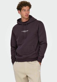 Hoodie violet foncé avec une poche avant, capuche à cordon et impression de texte blanche. Fabriqué en tissu doux, il a une coupe décontractée.
