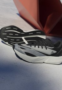 Čierne a šedé športové topánky s elegantným dizajnom, štruktúrovaným zvrškom a flexibilnou podrážkou. Obsahujú značkové akcenty a charakteristický vzor behúňa.