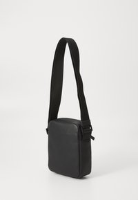 Black leather crossbody bag with a textured surface, square shape, and adjustable fabric strap. Features minimalistic design with no visible hardware.