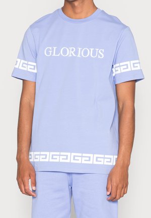 T-shirt en coton bleu clair avec "GLORIOUS" imprimé en blanc, avec un motif géométrique blanc sur les manches et l'ourlet inférieur.