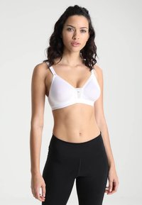 Hvit trådløs BH med trekantede kopper, blondekant i midten, justerbare stropper og glatt tekstur; kombinert med svarte høyhals leggings.