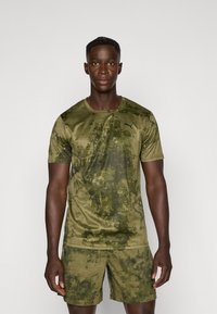 Olijfgroene sportt-shirt en shorts met een gestructureerd camouflagepatroon. Gemaakt van lichte stof en heeft het Puma-logo op de borst.