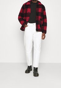 Red and black checkered fleece jacket with a collar, paired with white trousers and black ankle boots, featuring a textured finish.
