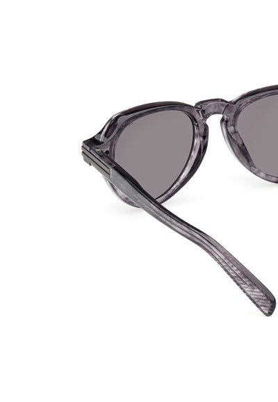 Szare, przezroczyste okulary przeciwsłoneczne w kształcie kocich oczu o kanciastym fasonie. Oprawki wykonane są z acetatu, z ciemnoszarymi soczewkami i fakturowanym zausznikami.