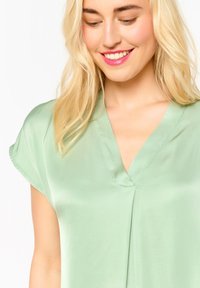 Mint green satin blouse with a V-neckline, short sleeves, and a relaxed fit. Smooth texture with subtle stitching detail along the neckline.