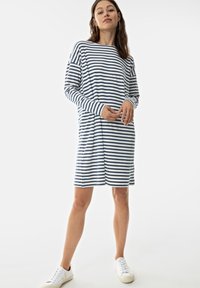 Abito a maniche lunghe a righe bianco e blu navy, con una vestibilità comoda e spacchi laterali. Abbinato a sneakers bianche per un look casual.