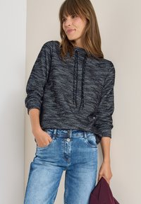 Felpa grigia scuro con maglia testurizzata, cappuccio con cordino e polsini a costine, abbinata a jeans blu chiaro in denim spazzolato.
