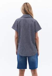 Kortärmad skjorta med krage i svartvitt rutmönster, kombinerad med blå denimshorts med fransade kanter och en avslappnad passform.