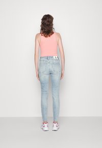 Ljusblå skinny jeans med hög midja, kombinerat med en ribbad rosa tanktop och vita sneakers med röda detaljer.