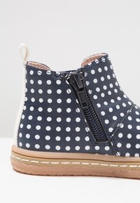 Bottes de cheville pour enfants bleu marine avec des pois blancs, zip latéral, tirant beige et semelle cousue marron clair.