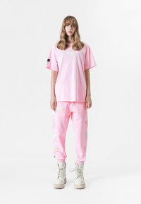 Camiseta rosa de gran tamaño y joggers a juego con acentos bordados en blanco, combinados con botas beige de cordones, con un ajuste relajado y textura suave.