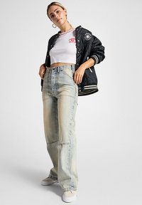 Chaqueta bomber acolchada negra con rayas blancas, camiseta blanca corta y jeans de pierna ancha de color azul claro. Incluye pendientes y zapatos blancos.