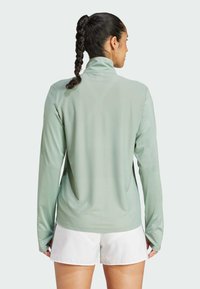Lichtgroen sporttop met lange mouwen en hoge kraag, voorzien van duimgaten, gemaakt van gladde, ademende stof en met een getailleerd silhouet.