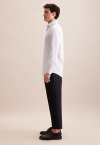 Lichtblauw gestreept overhemd met lange mouwen en knoopmanchetten, gecombineerd met zwarte op maat gemaakte broek en zwarte veterschoenen. Eenvoudige, moderne silhouet.