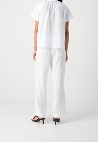 Haut blanc à manches courtes en lin avec encolure froncée, associé à un pantalon large en lin blanc, et des sandales à talons noires.