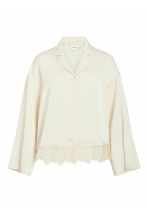 Krēmveida blūze ar atloku apkakli, pogu aizdari un garām piedurknēm. Apakšmalā dekoratīvs mežģīņu apmales elements. Mīksts, gluds audums.