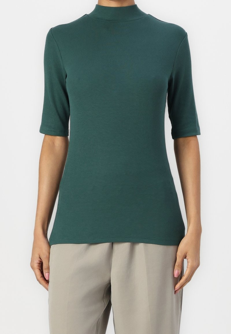 Haut en tricot côtelé teal avec un col haut et des manches courtes, présentant une silhouette ajustée et une texture lisse.