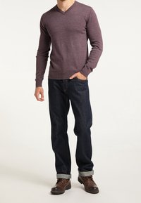 Sweter z dekoltem w serek, z długim rękawem w ciemnofioletowym kolorze, zestawiony z ciemnoniebieskimi dżinsami, podwiniętymi mankietami i brązowymi skórzanymi butami.