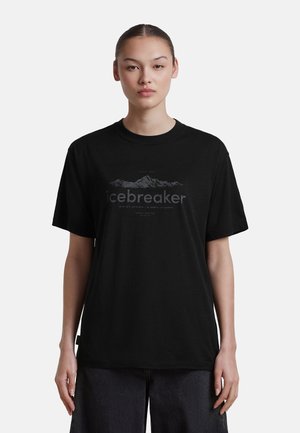 Frau mit zurückgebundenen Haaren trägt ein schwarzes T-Shirt mit einem Bergmotiv und dem Wort "icebreaker" auf der Vorderseite.