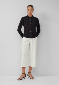 Zwarte blouse met lange mouwen en knopen, voorzien van een kraag, gecombineerd met witte cropped broeken en zwarte sandaalschoenen met hakken, met een gladde textuur.
