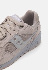 Light gray sneaker featuring a mix of suede and mesh materials, round laces, a textured sole, and a subtle logo accent on the side.
