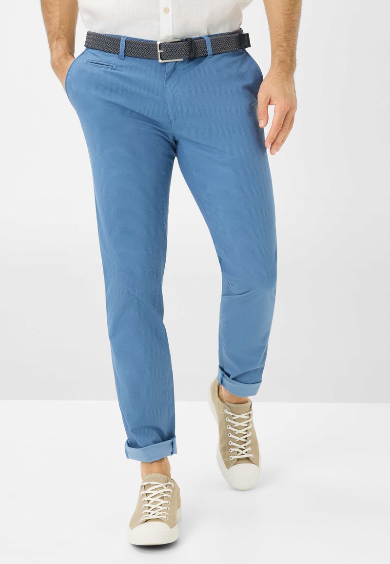 Chinos en coton bleu avec une finition texturée, présentant une coupe slim et des ourlets roulés. Associés à des baskets décontractées beiges.