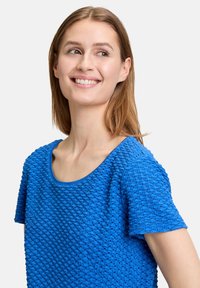 Blaues gestricktes Kurzarmoberteil mit strukturiertem Muster und rundem Ausschnitt, mit einem leicht lockeren Schnitt und leichtem Material.