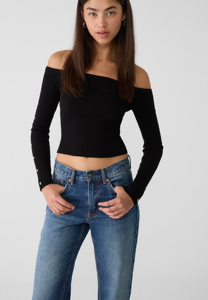 Top lungo a maniche lunghe a coste nera spalle scoperte abbinato a jeans chiari a vita alta con dettagli di bottoni e tasche.