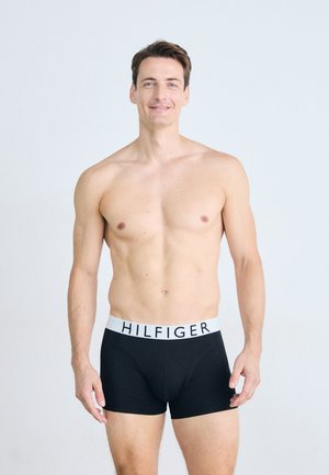 Schwarze Boxershorts mit einem weißen Bündchen, auf dem der Text "HILFIGER" steht. Der Stoff ist glatt und das Design ist figurbetont.