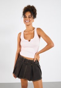 Ljusrosa crop top med rundad halsringning, kombinerad med en svart denimkjol med veck och slitna kanter samt synliga sömnadsdetaljer.