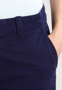 Shorts en coton bleu marine avec une taille plate, des poches latérales et une texture subtile. Coupe droite avec des détails de couture minimalistes.