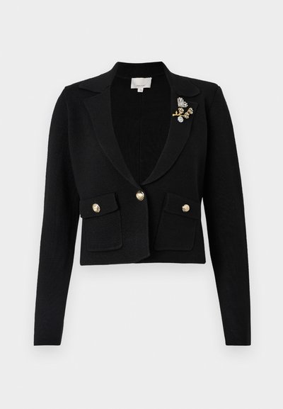 Μαύρη κοντή σακάκι με υφή πλέξης, με γιακά σε σχήμα V, δύο μπροστινές τσέπες, χρυσά κουμπιά και διακοσμητική καρφίτσα.