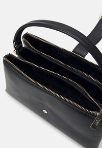 Sac à main DKNY en cuir noir avec deux compartiments à fermeture éclair, détails de fermetures éclair dorées et une poignée courte.