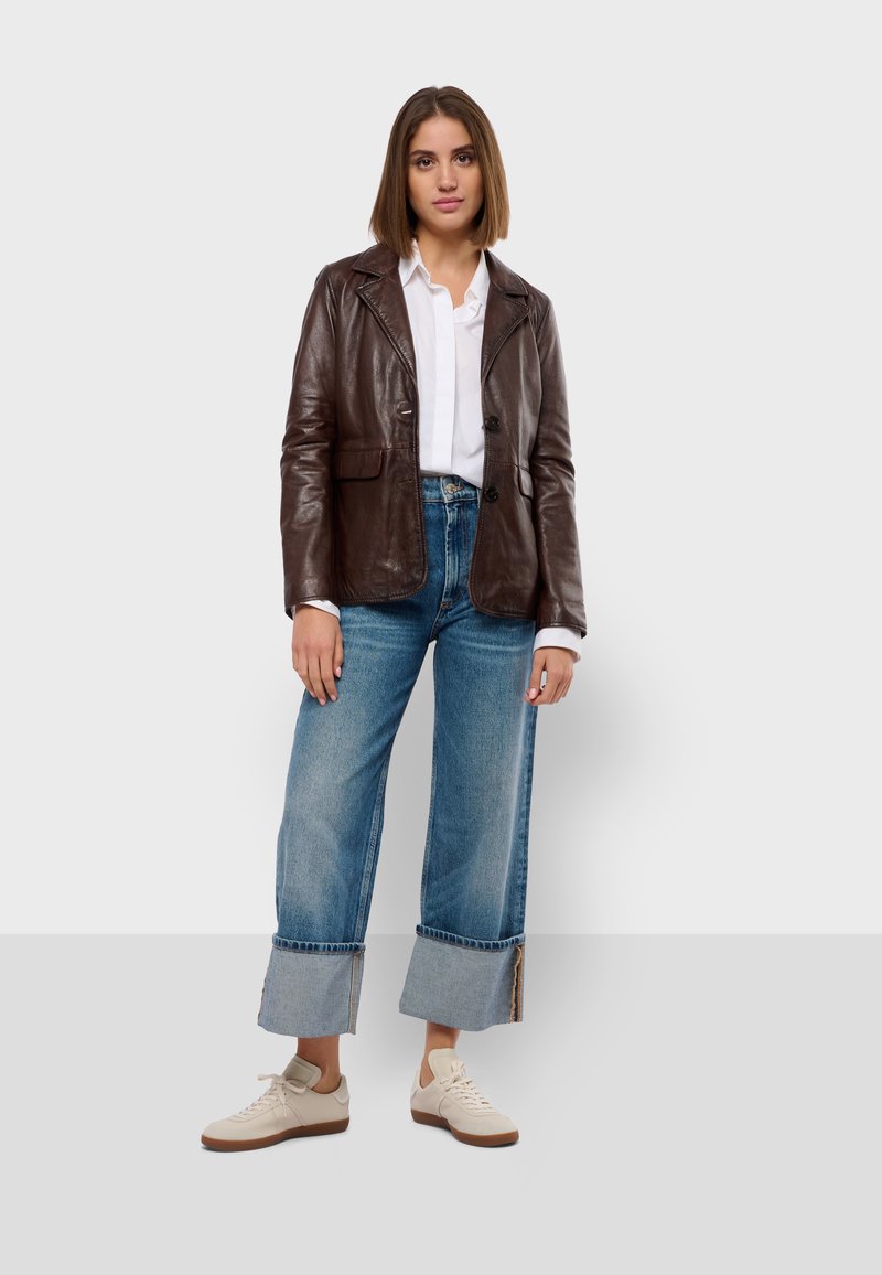 Blazer in pelle marrone, camicia bianca, jeans a gamba larga blu chiaro con orli sfilacciati, sneakers beige con suola marrone.