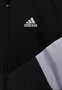 Black and gray athletic jacket with a zip closure, featuring a triangular design and a prominent white adidas logo on the chest.