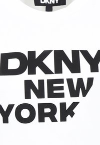Camiseta blanca con letras negras en negrita que dicen "DKNY NEW YORK". El tejido parece suave con un diseño clásico de cuello redondo.