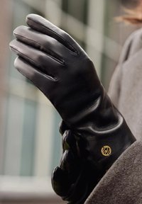 Gants en cuir noir au design épuré, dotés de trois lignes de couture sur les doigts et d'un accent en or près du poignet.