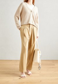 Cardigan lavorato a maglia beige, scollo a V, con bottoni frontali; pantaloni beige a gamba larga su misura; sandali bianchi con cinturini; borsa color crema con una sciarpa a fantasia.