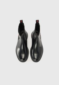 Black leather chelsea boots with elastic side panels, smooth texture, rounded toe, and red pull tab. Minimalist design, flat rubber sole.