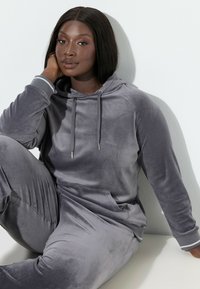 Szary welurowy komplet do noszenia w domu składający się z bluzy z kapturem i sznurkami oraz dopasowanych spodni. Miękka faktura z delikatnym paskowaniem na mankietach.