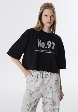 Camiseta negra corta con mangas cortas que presenta el texto "No. 97" en una fuente en negrita. Combinada con pantalones gris claro adornados con varios patrones.