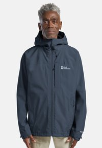Giubbotto impermeabile navy con cappuccio, chiusura zip frontale e logo sul petto. Presenta polsini regolabili e un tessuto leggero e morbido.