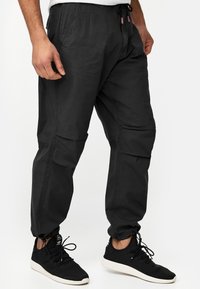 Pantalones cargo negros hechos de una tela duradera, con puños elásticos, múltiples bolsillos y cintura con cordón para un ajuste personalizable.