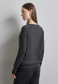 Maglione grigio scuro, dalla vestibilità ampia, con una maglia testurizzata, scollo rotondo e polsini a costine, abbinato a jeans neri.