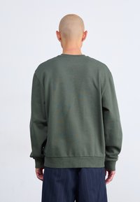 Sudadera verde hecha de tela suave, con cuello redondo, mangas largas, puños acanalados y un corte relajado, combinada con pantalones de rayas en navy.