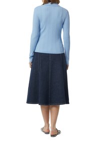 Hellblau gestreifter Pullover mit langen Ärmeln, kombiniert mit einem dunkelblauen Denim-A-Linienrock mit kontrastierenden Nähten. Flache schwarz-weiße Sandalen.